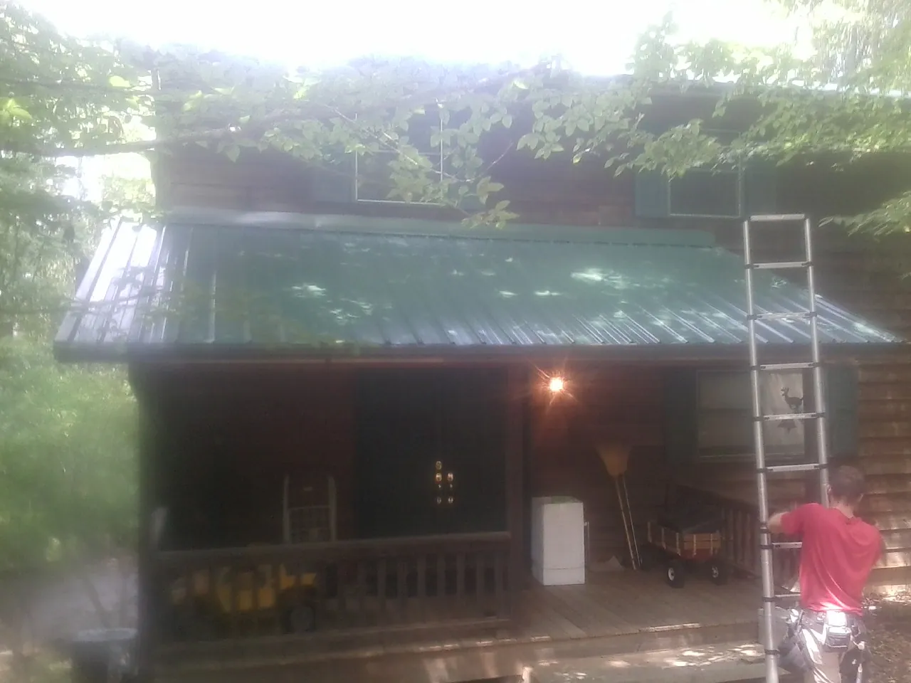 Worker on a ladder at the green porch roof of a wooded cabin in Akron